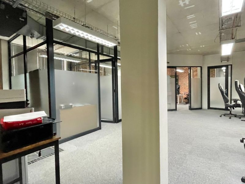 Modern open-plan office space featuring glass partitioned rooms, exposed industrial-style ceilings, and carpeted flooring.