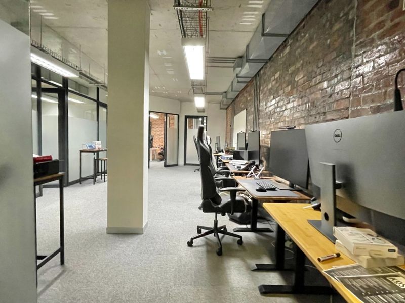 Modern industrial-style office space featuring exposed brick walls, concrete ceilings, and glass partitions, providing an open and professional work environment.