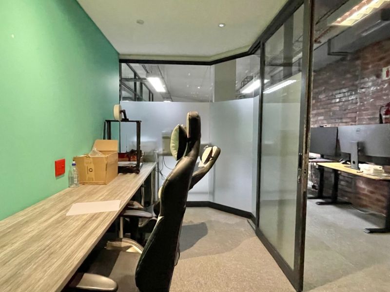 A modern office space featuring a built-in desk, glass partitioning, and an exposed brick wall, providing a contemporary industrial aesthetic.