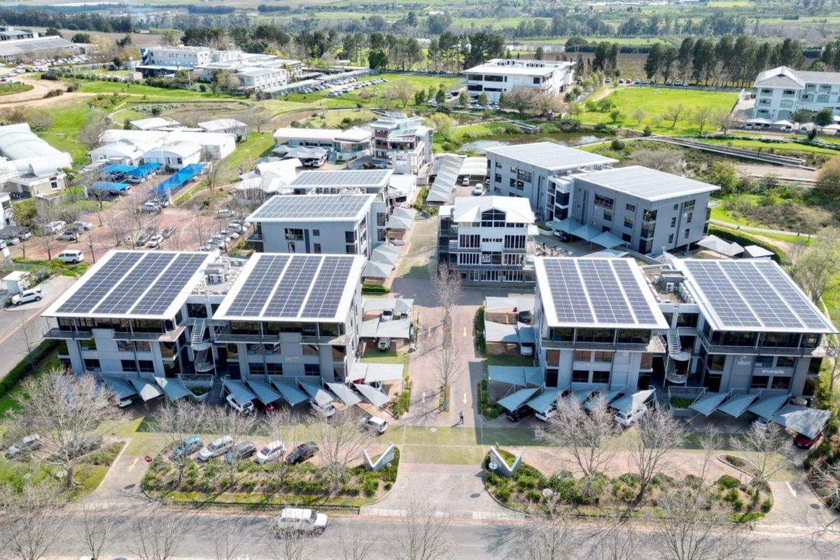 Aerial view of a modern office park complex featuring multiple buildings with rooftop solar installations and extensive paved parking facilities.
