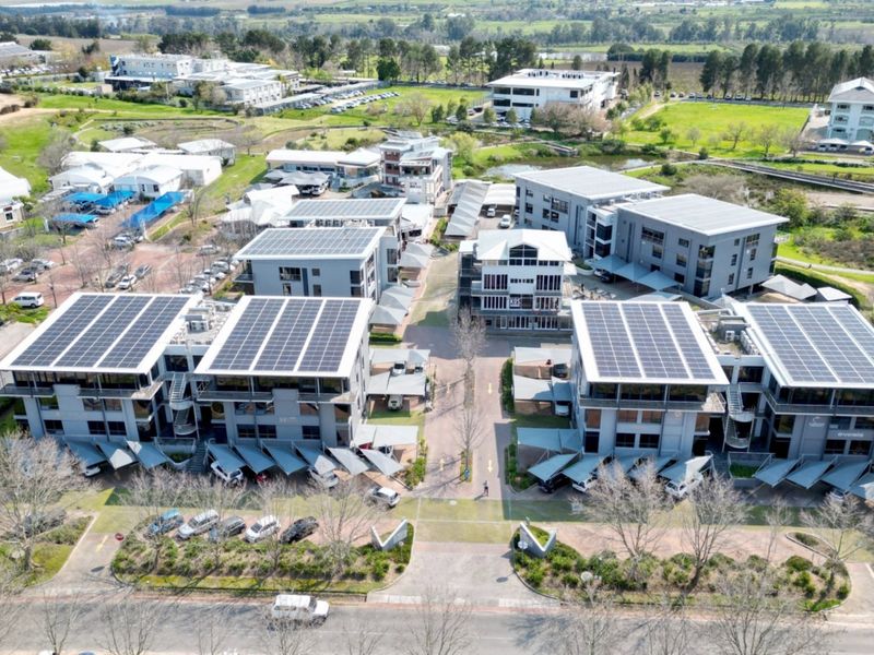 Aerial view of a modern office park complex featuring multiple buildings with rooftop solar installations and extensive paved parking facilities.