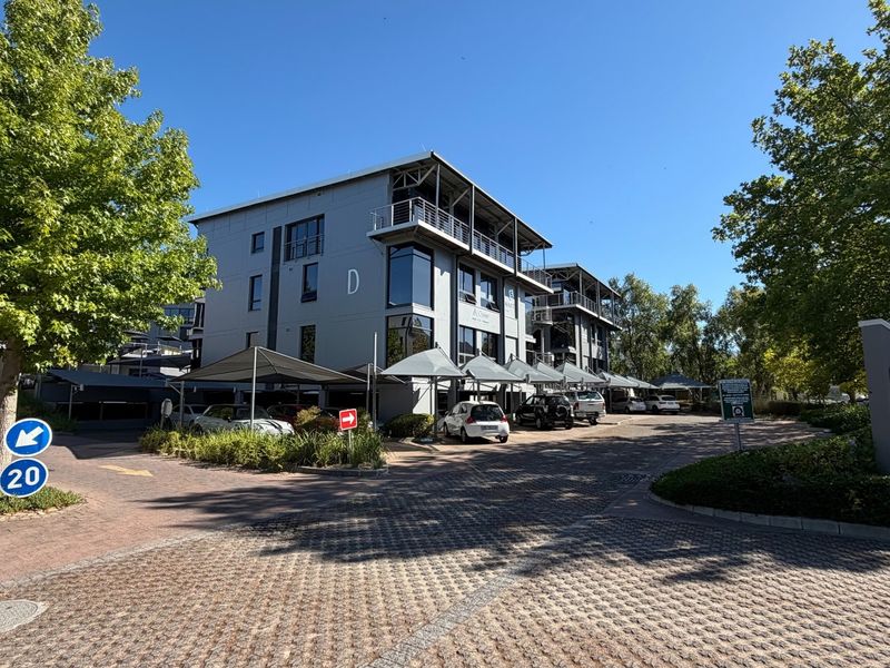 Exterior view of a modern multi-story office building featuring paved driveway access and covered parking facilities.