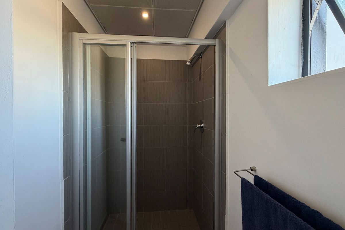 A clean and functional bathroom featuring a modern shower enclosure with tiled walls and a drop ceiling.