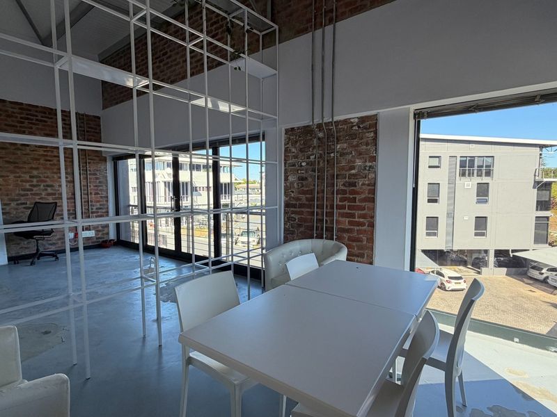 Modern industrial-style office space featuring exposed brick walls, polished concrete floors, and a large metal partition, offering ample natural light.