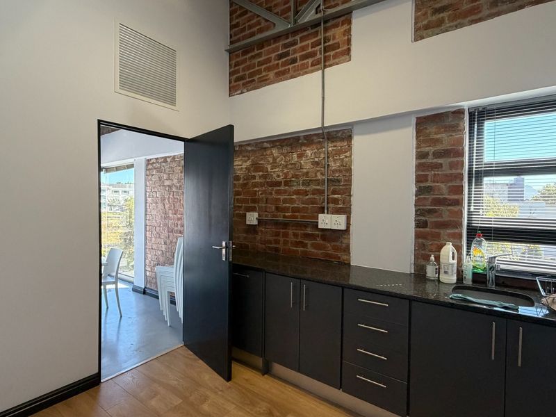 Modern kitchen area featuring exposed brick walls, dark cabinetry with granite countertops, and an industrial-style exposed ceiling truss.