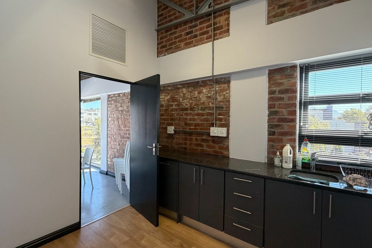Modern kitchen area featuring exposed brick walls, dark cabinetry with granite countertops, and an industrial-style exposed ceiling truss.