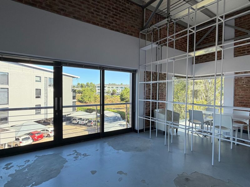 Modern industrial-style office space featuring exposed brick walls, polished concrete floors, and large sliding glass doors leading to a balcony.