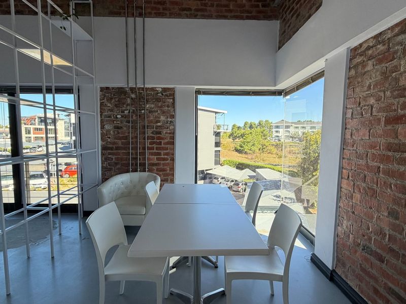 Modern office space featuring exposed brick walls, large windows with natural light, and an open-plan layout suitable for a professional work environment.
