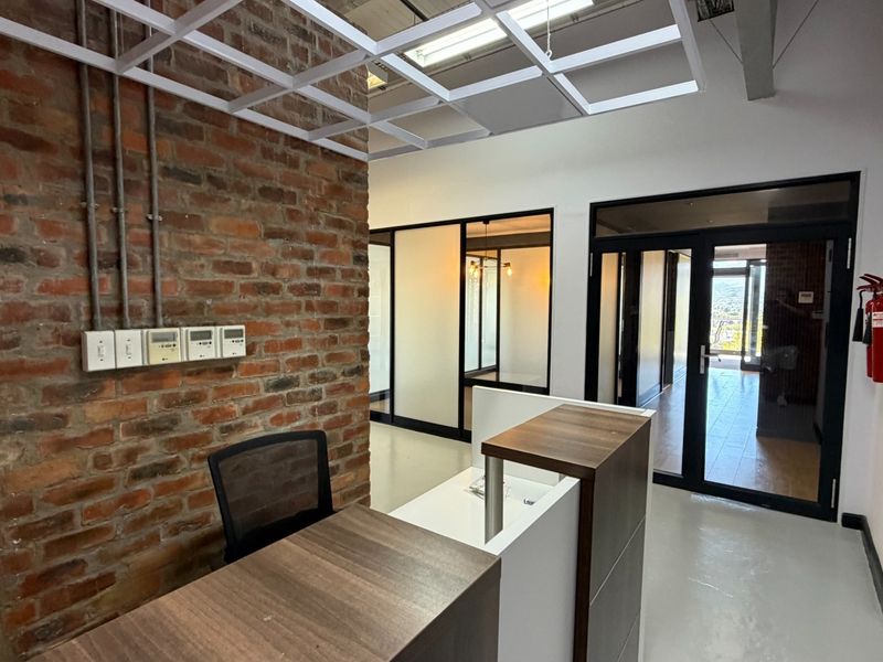 Modern office reception area featuring exposed brickwork, glass partitioning, and a contemporary suspended ceiling grid with polished flooring.