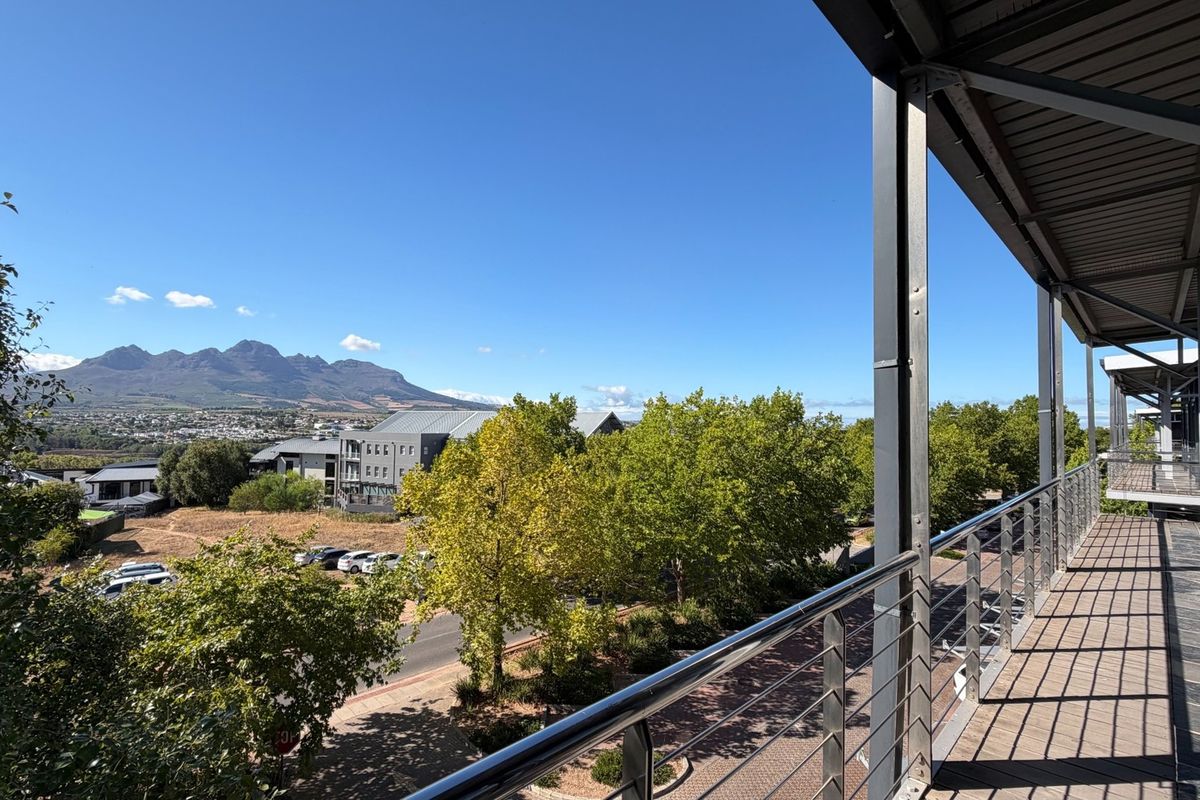 A spacious covered balcony featuring modern metal railings and tiled flooring, offering expansive views of the surrounding landscape and mountain range.