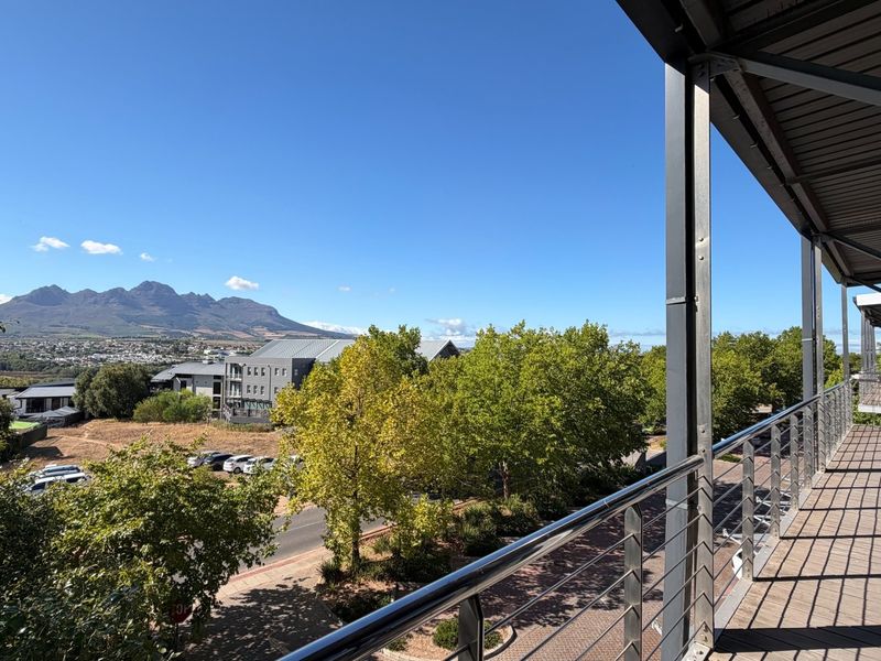 A spacious covered balcony featuring modern metal railings and tiled flooring, offering expansive views of the surrounding landscape and mountain range.