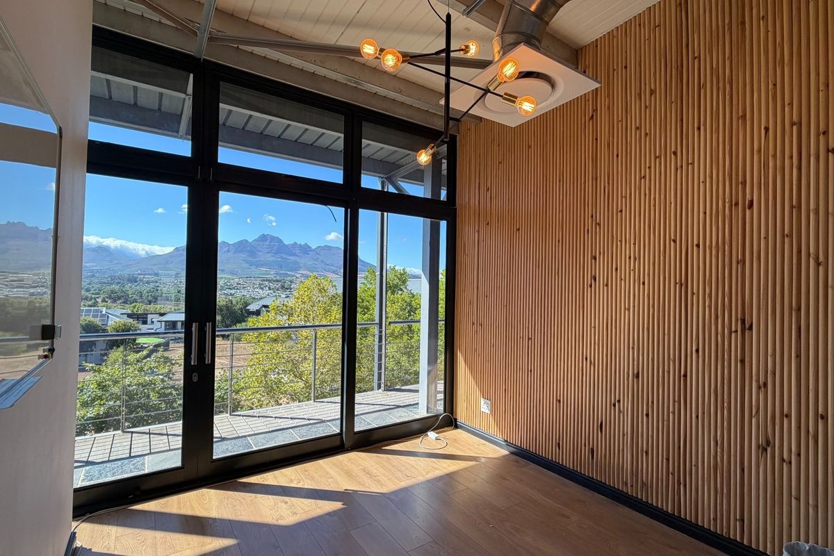 Modern office space featuring timber slat wall cladding, laminate flooring, exposed ceiling services, and large glass doors opening to a balcony with mountain views.