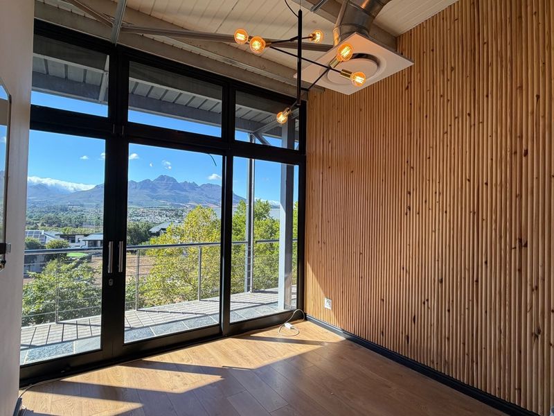 Modern office space featuring timber slat wall cladding, laminate flooring, exposed ceiling services, and large glass doors opening to a balcony with mountain views.
