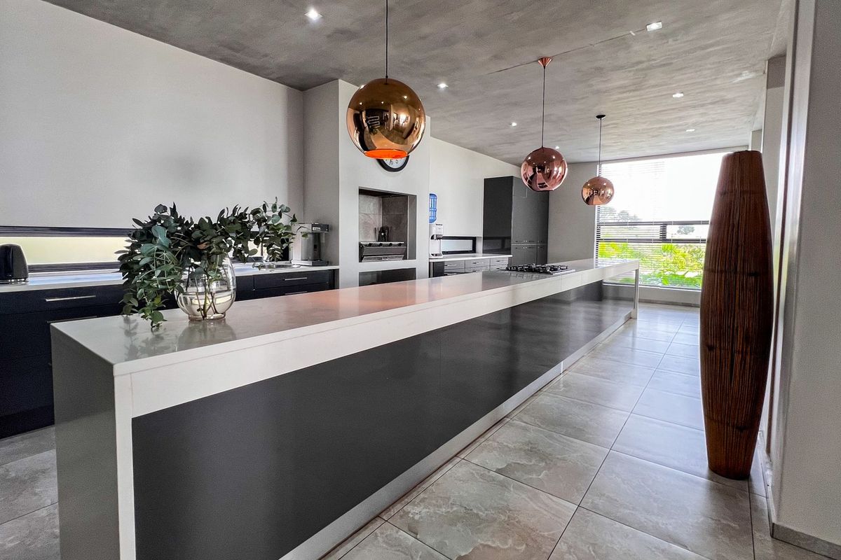 Modern kitchen featuring a long central island with stone countertops, built-in cooking appliances, and contemporary pendant lighting in a spacious, open-plan layout.