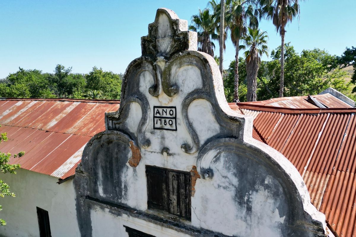 Aerial view of a historic Cape Dutch gable dated 1780, featuring traditional architectural detailing and a weathered corrugated iron roof structure.