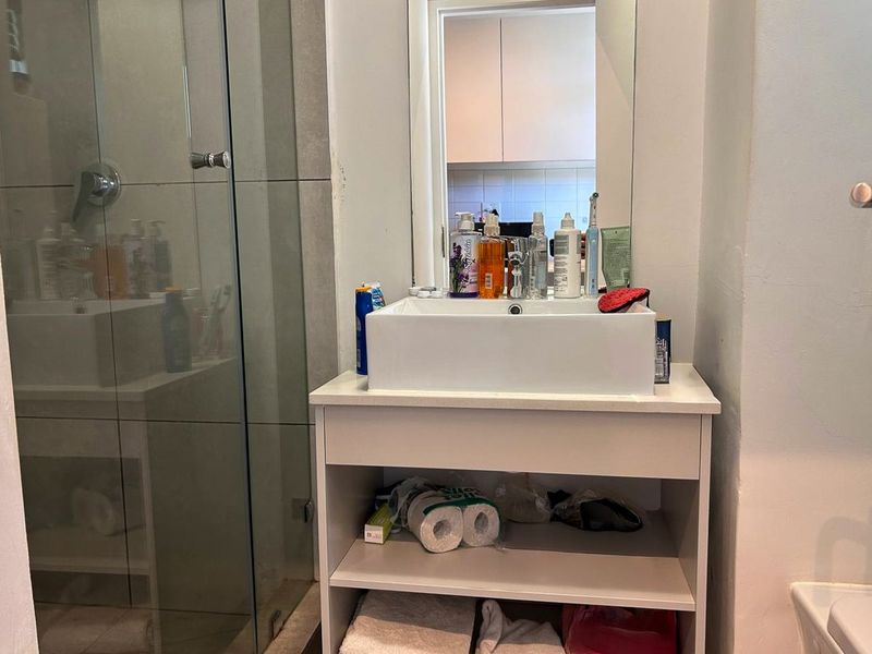 A compact bathroom featuring a modern vessel sink on a vanity cabinet, a glass-enclosed shower, and a wall-mounted mirror.