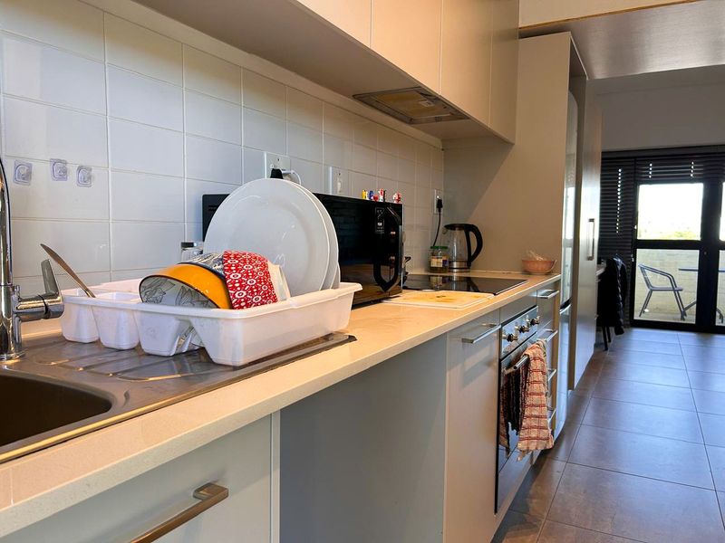 Modern kitchen featuring sleek cabinetry, stone countertops, integrated oven and hob, and tiled backsplash, leading to an open-plan living area.