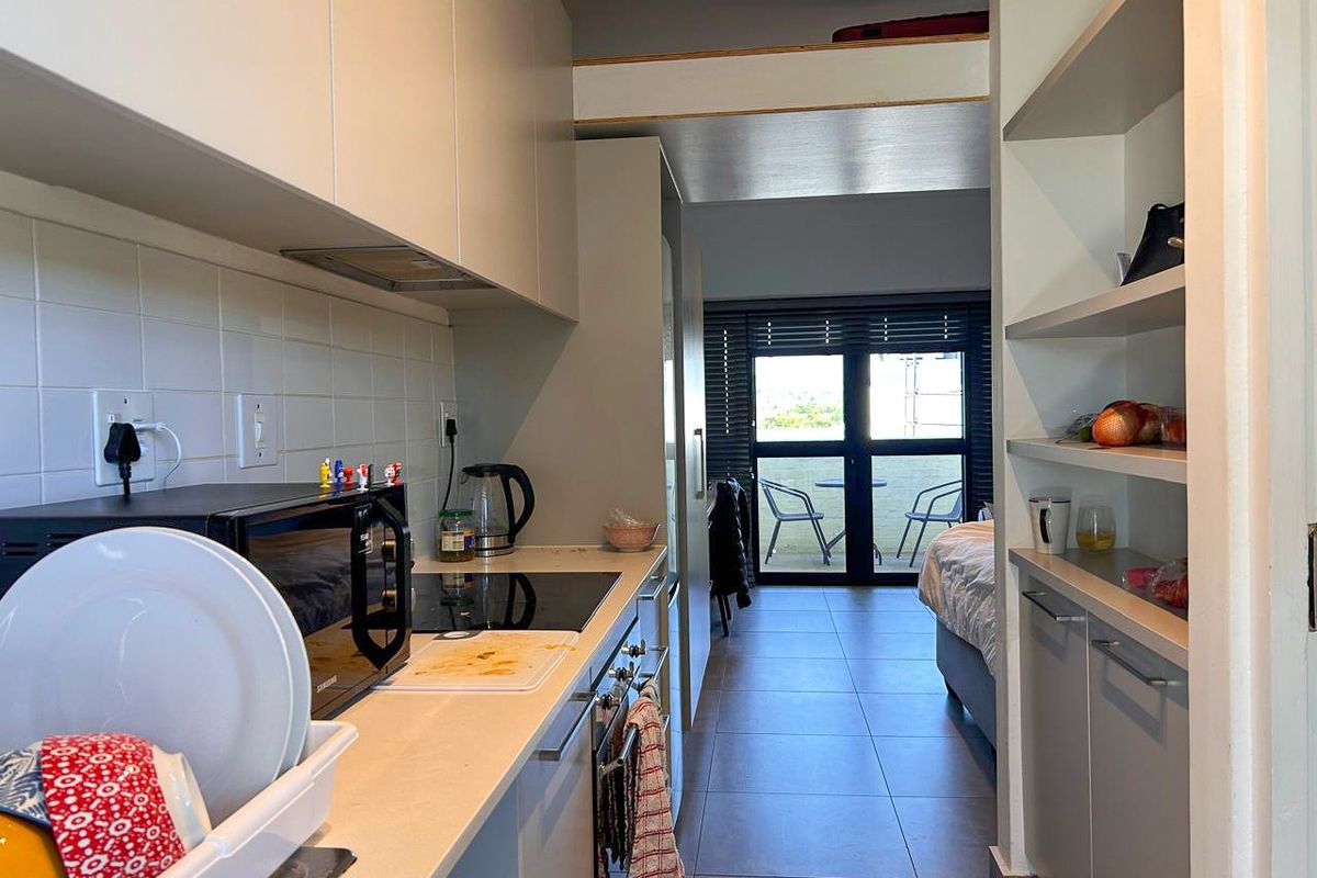 Compact galley-style kitchen featuring modern cabinetry, integrated appliances, and a tiled backsplash, leading directly into an open-plan living area with balcony access.