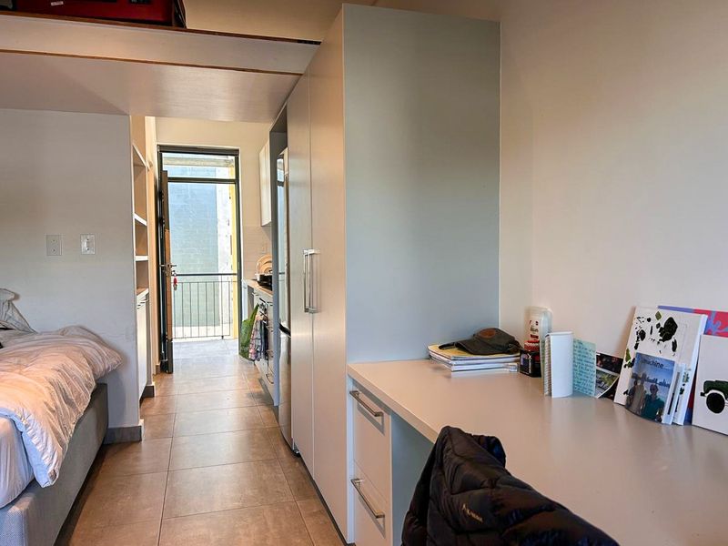 Open-plan studio apartment featuring a built-in desk, integrated cabinetry, tiled flooring, and direct access to a private balcony.