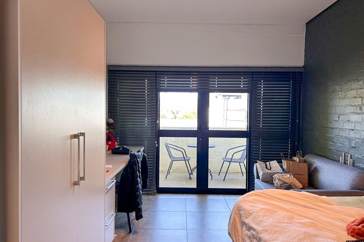 Bedroom featuring a built-in wardrobe, tiled flooring, a dark painted brick feature wall, and direct access to a private balcony through sliding glass doors.