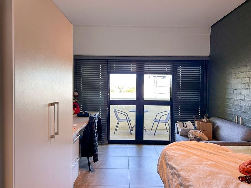 Bedroom featuring a built-in wardrobe, tiled flooring, a dark painted brick feature wall, and direct access to a private balcony through sliding glass doors.