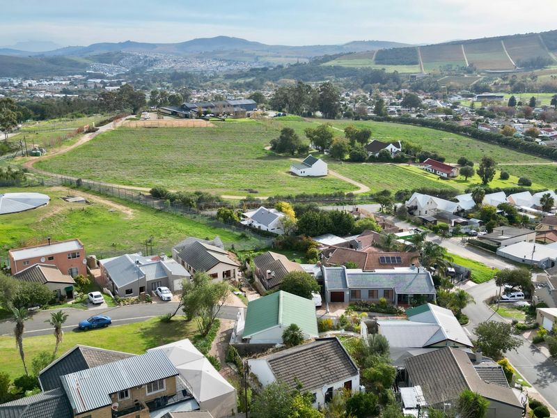 An aerial view of a residential neighborhood featuring various homes with tiled roofs, solar panels, and surrounding green landscape.