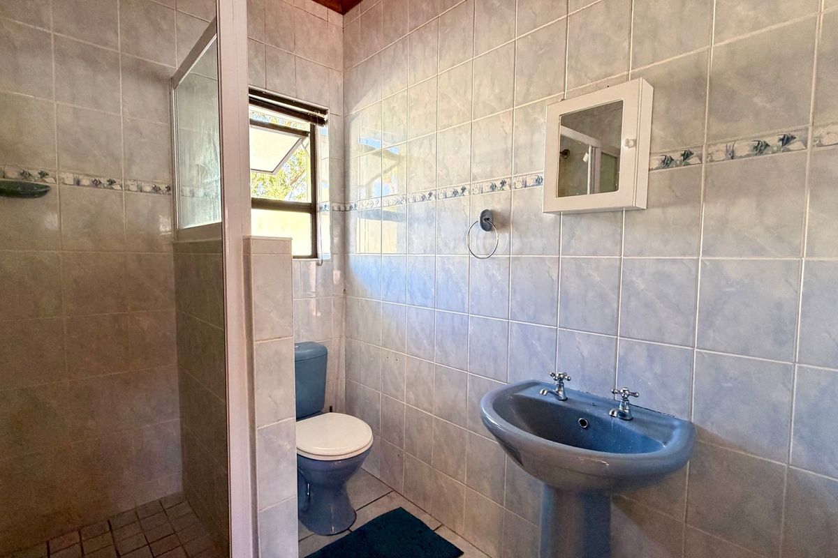 A functional bathroom featuring a pedestal basin, toilet, and shower enclosure with full-height wall tiling.