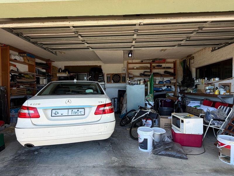 A spacious double garage featuring a sectional door, concrete flooring, and built-in storage shelving, offering ample space for vehicle parking and workshop use.