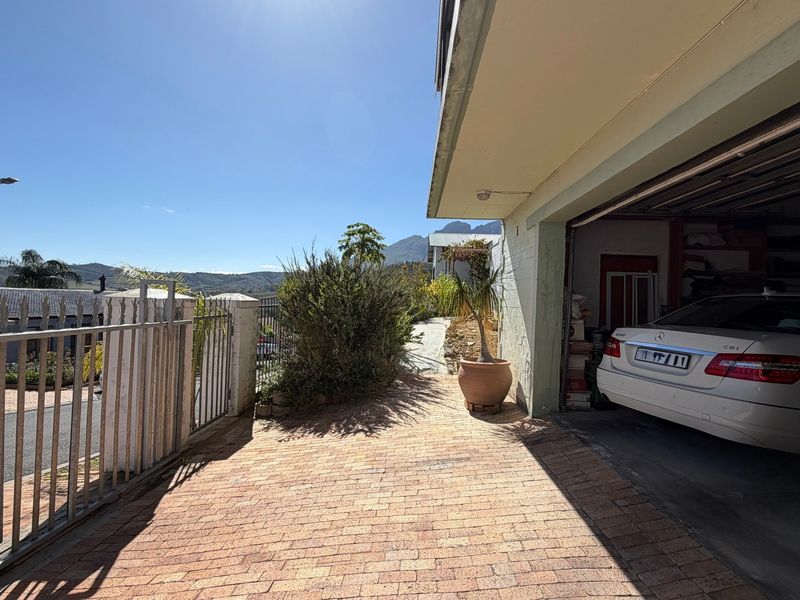 Exterior view of a residential garage with a paved driveway and metal security fencing, featuring mountain views in the background.