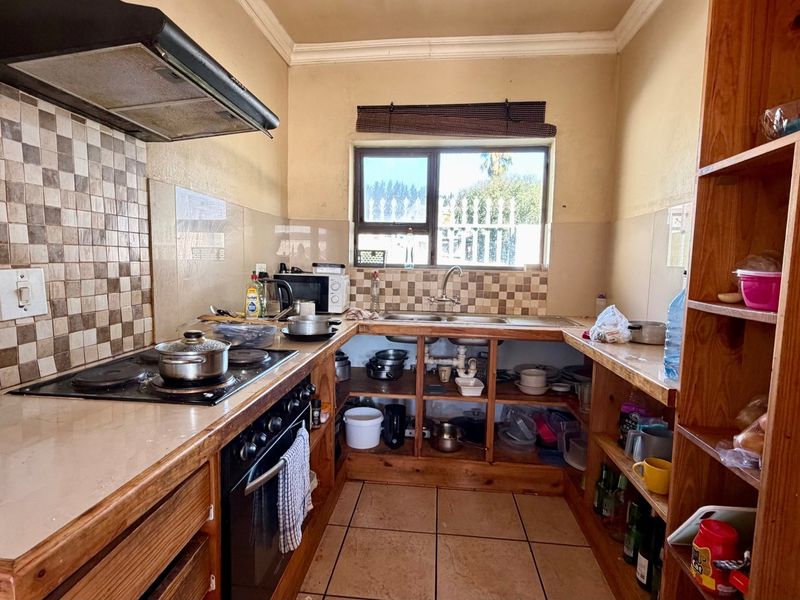A functional kitchen featuring built-in wooden cabinetry, an electric hob with extractor fan, and a double sink with tiled splashback.