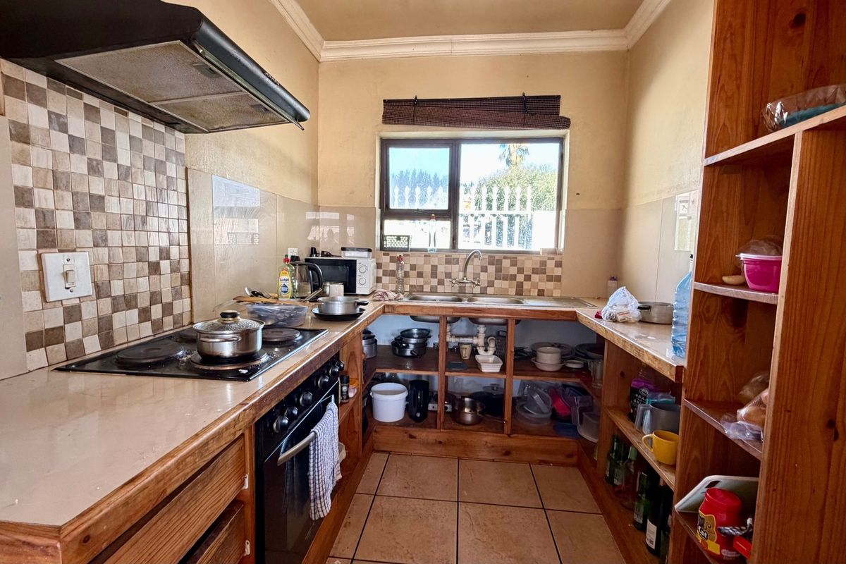 A functional kitchen featuring built-in wooden cabinetry, an electric hob with extractor fan, and a double sink with tiled splashback.