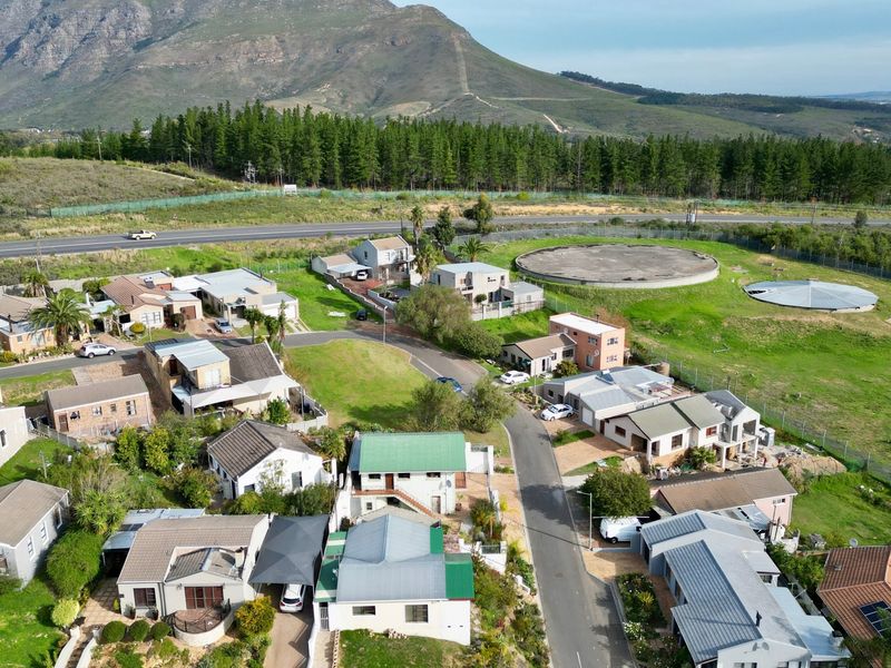 An aerial view of a residential housing estate featuring multiple homes, paved streets, and large water storage reservoirs set against a mountain backdrop.