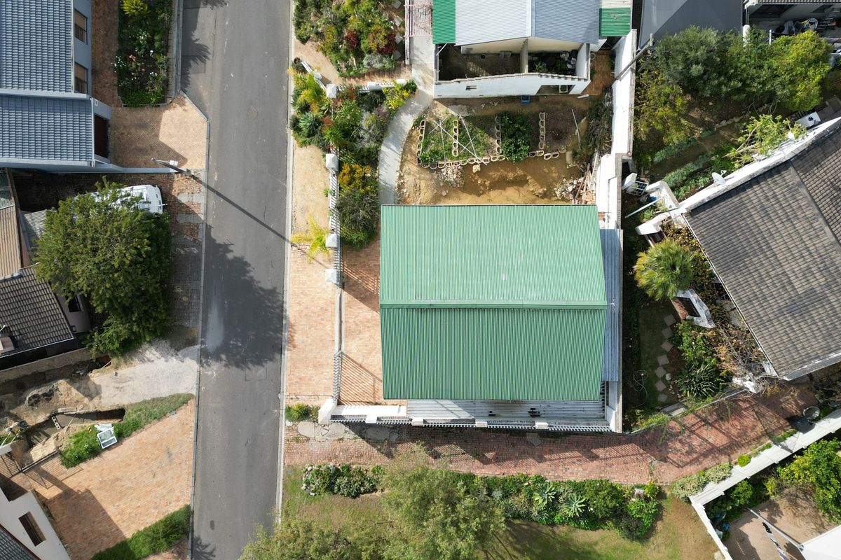 Aerial view of the property showing the green metal roof, paved driveway, and surrounding garden area.