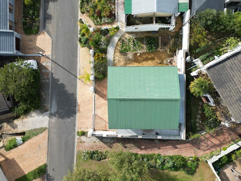 Aerial view of the property showing the green metal roof, paved driveway, and surrounding garden area.