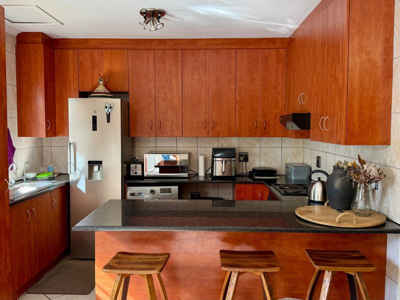 A functional kitchen featuring warm-toned wooden cabinetry, granite countertops, a breakfast bar, and a tiled backsplash with integrated cooking appliances.