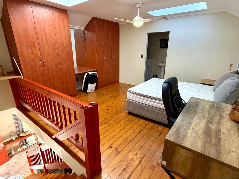 Spacious loft-style bedroom featuring polished timber flooring, built-in cabinetry, dual skylights, and an open-plan layout overlooking the lower level.