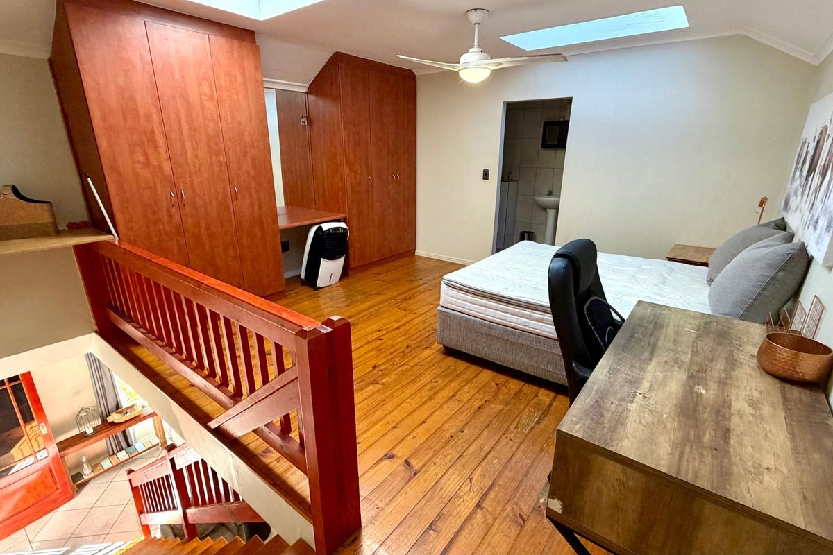 Spacious loft-style bedroom featuring polished timber flooring, built-in cabinetry, dual skylights, and an open-plan layout overlooking the lower level.
