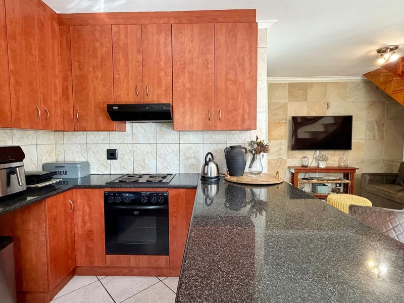Open-plan kitchen featuring granite countertops, wooden cabinetry, and a built-in oven, flowing into a living area with a stone feature wall and wooden staircase.