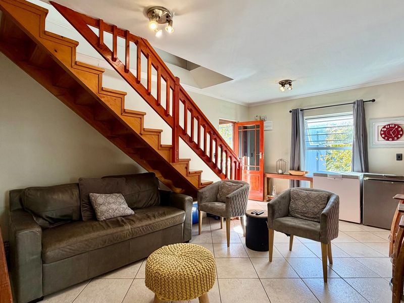 Open plan living area featuring a prominent wooden staircase, tiled flooring, and direct access to an exterior door.