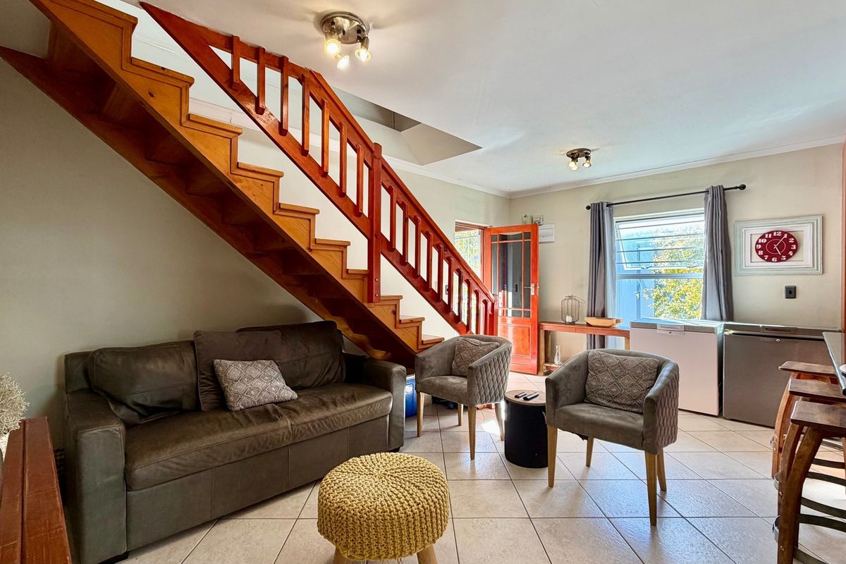 Open plan living area featuring a prominent wooden staircase, tiled flooring, and direct access to an exterior door.