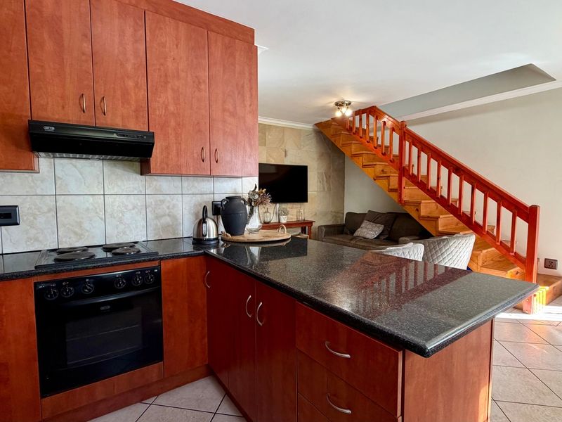 Open-plan kitchen featuring wooden cabinetry, granite countertops, and integrated appliances, seamlessly flowing into the living area with a wooden staircase.