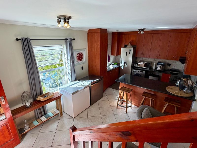 A functional kitchen featuring warm-toned wooden cabinetry, granite countertops, a breakfast bar, and tiled flooring, viewed from an elevated position.