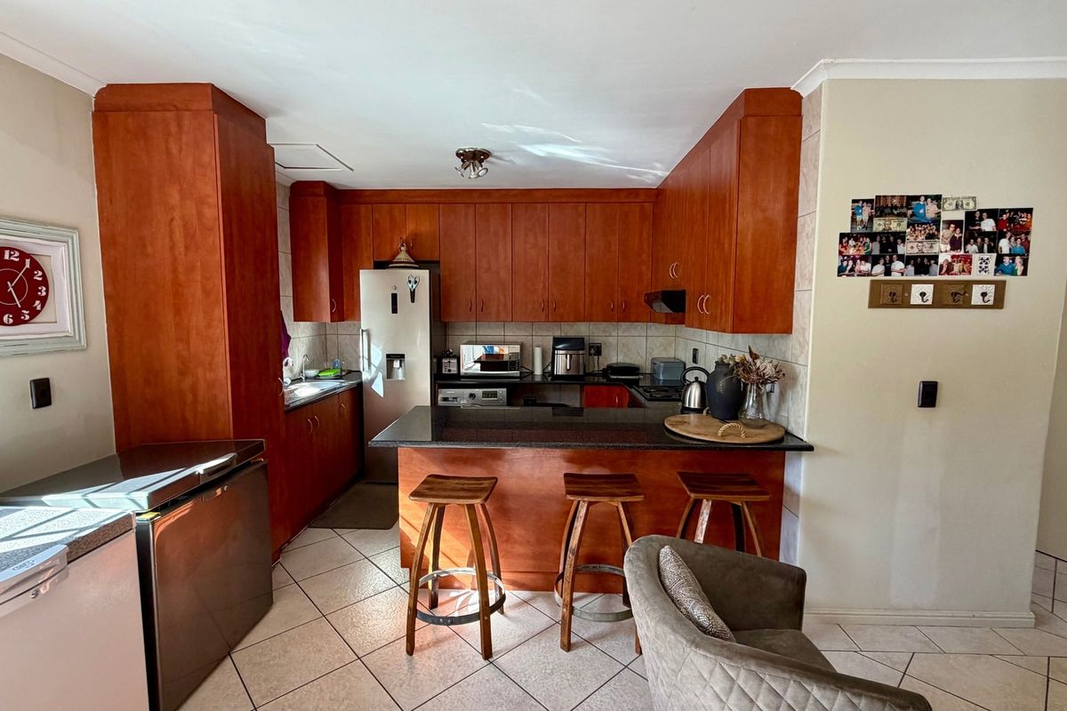A functional kitchen featuring warm-toned built-in cabinetry, granite countertops, a breakfast bar, and ceramic tile flooring, offering a practical layout for daily use.