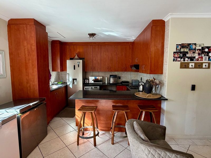 A functional kitchen featuring warm-toned built-in cabinetry, granite countertops, a breakfast bar, and ceramic tile flooring, offering a practical layout for daily use.