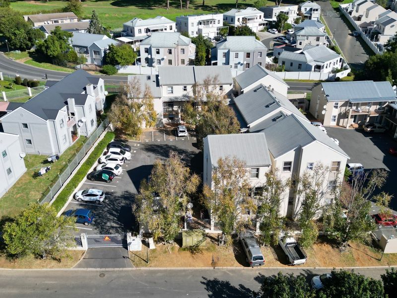 Aerial view of an apartment complex featuring multiple residential buildings, paved parking areas, and perimeter security fencing.