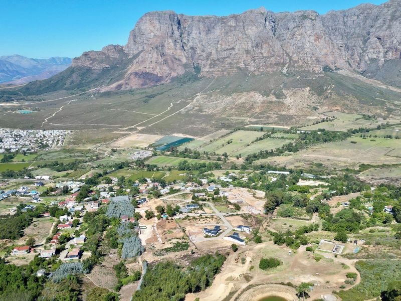 An aerial view of a residential development area set against a prominent mountain range, showcasing the surrounding landscape and local infrastructure.