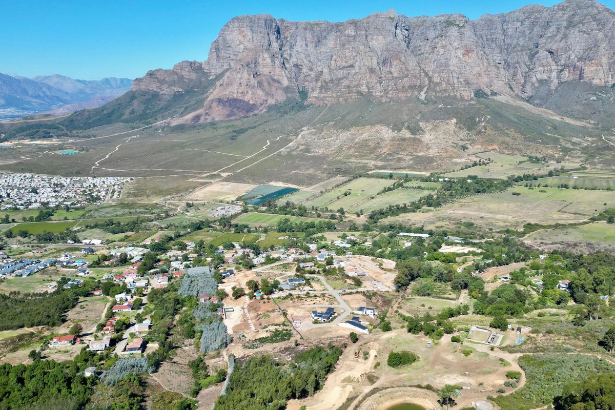 An aerial view of a residential development area set against a prominent mountain range, showcasing the surrounding landscape and local infrastructure.
