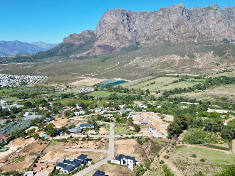 Aerial view of a residential development site set against a scenic mountain backdrop, showcasing the surrounding landscape and established road infrastructure.