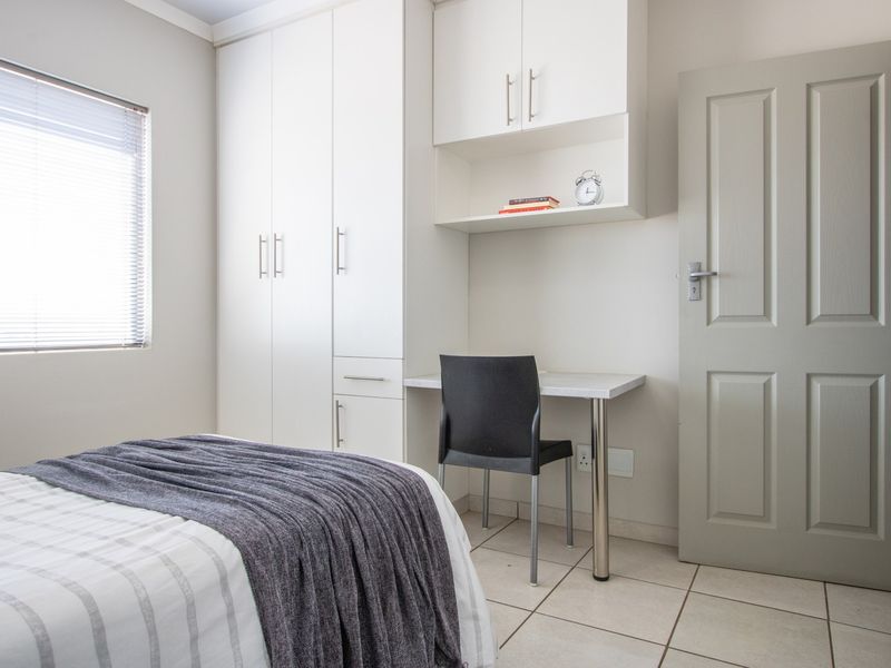 A well-maintained bedroom featuring built-in cupboards, a integrated desk workspace, tiled flooring, and neutral finishes.