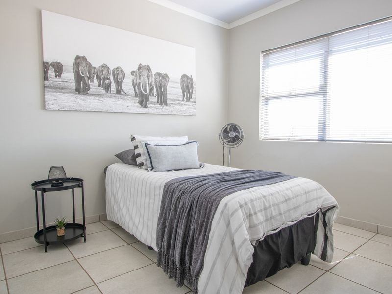 A well-lit bedroom featuring neutral wall tones, tiled flooring, and venetian blinds, providing a clean and functional living space.